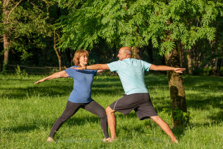 Mature couple practising yoga position with arms open standing in the park for healthy lifestyleの写真素材