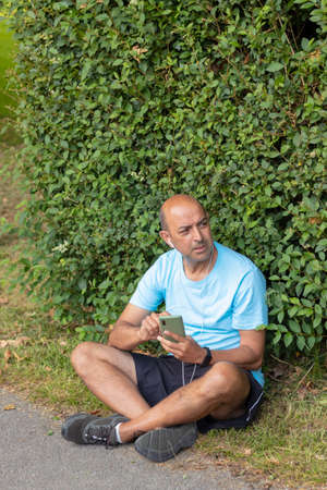 Bald man getting tired after a hard day of sport taking a break to catch his breath while listening to musicの写真素材