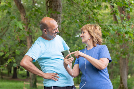 Adult couple laughing at a photo on their smartphone while resting from exercising in the city parkの写真素材