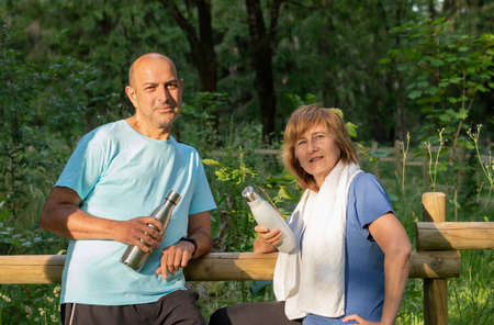 Mature couple leaninglooking to camera after doing exercise in the park holding reusable metal bottlesの写真素材