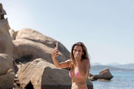 Beautiful brunette young influencer woman laughing and having fun while taking pictures at the beachの写真素材