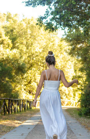 Vertical view of unrecognizable young brunette woman dancing into the nature whearing white dressの写真素材
