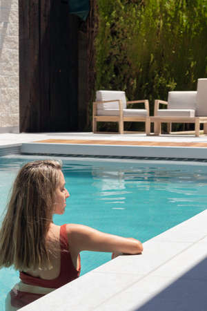 Backwards view of young blonde woman relaxing in the swimming pool on a hot summer dayの写真素材