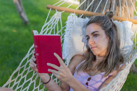 Young beautiful woman reading a book realaxing from work in a hammock outdoors in natureの写真素材