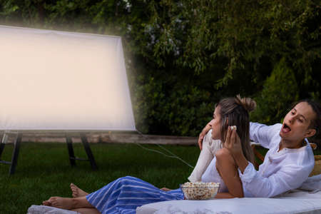 Young couple in the park watching a summer movie. Boyfriend stealing opcorns from behind to his girlfriendの写真素材