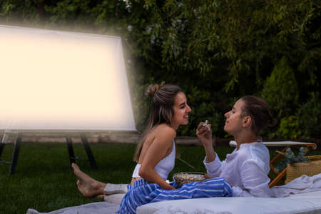 Happy and smiling girlfriend and boyfriend eating popcorns together in the outdoor cinema in summerの写真素材