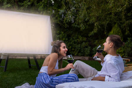 In love young couple laughing and having fun while drinking red wine and watching a movie as a dateの写真素材
