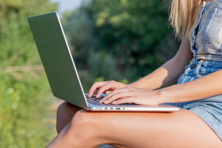 Unrecognizable young blonde woman working on her laptop sorrounded by nature in summer timeの写真素材