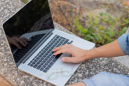 Close up view of unrecognizable young man working on his laptop with hand and eyeglasses on top of...