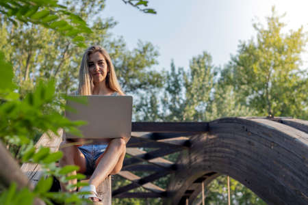 Young woman looking to camera while working on her laptop as a blogger and digital nomad with copy...