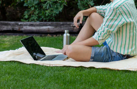 Unrecognizable young man sitting in the garden using the computer in his leisure time in summerの写真素材