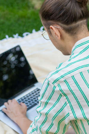 Vertical back view with selective focus of man working as freelancer on laptop in the home gardenの写真素材
