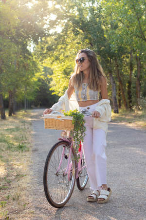 Vertical view of young woman looking to the side on a pink retro bicycle sorrounded by nature in springの写真素材