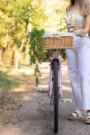 Vertical view of standing unrecognizable young woman with a bike on the side in the road sorrounded by natureの写真素材