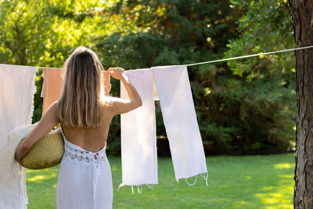 Back view of unrecognizable young woman on boho outfit hanging up the washing in the summer gardenの写真素材