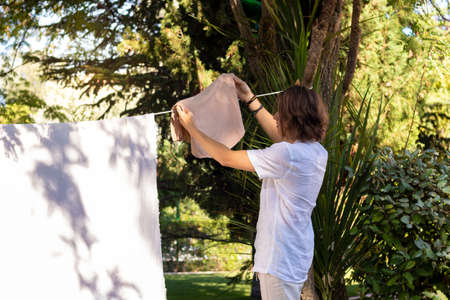 Young unrecognizable man from the back hanging out the washing in the home garden in summer timeの写真素材