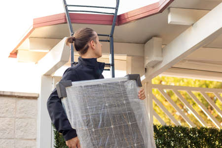 Side view of young electrician on a stair installing solar panels in the roof of a house as clean energyの写真素材