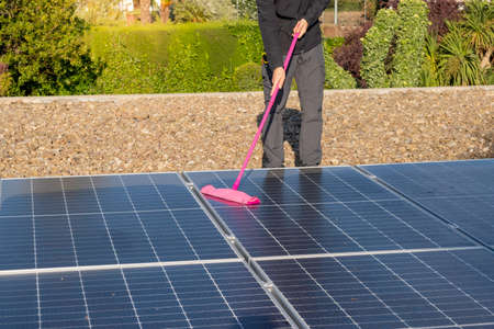 Unrecognizable man cleaning with a mop a solar panel pant installation in the roof of the houseの写真素材