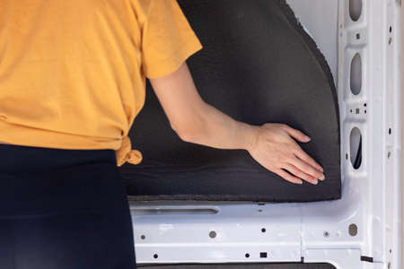 Close up view of unrecognizable young woman building a self made RV camper van while applying the rubber isolationの写真素材