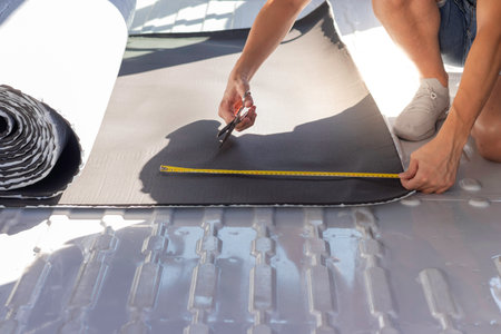 Unrecognizable young man measuring and cutting the rubber isolation roll for the insulation of a...