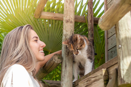 Happy and smiling young woman with cute cat playing in the garden on a wooden boothの写真素材