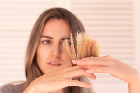 Selective focus of split ends in blond hair holded by blurred young woman in the backgroundの写真素材