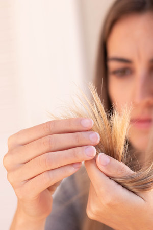Vertical close up view of frustated cropped young woman looking and touching her blond damage hair selective focusの写真素材