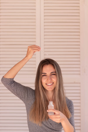 Vertical view of happy young woman with blond hair putting anti hair loss serum on hair in fall timeの写真素材