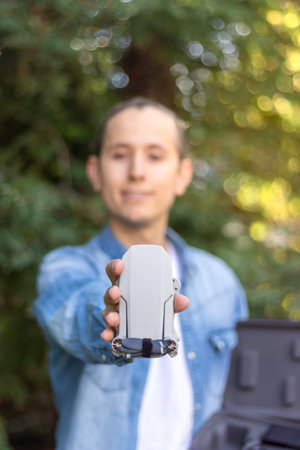 Selective focus of a small folded drone held by the hands of a young man dressed in denim clothes in...