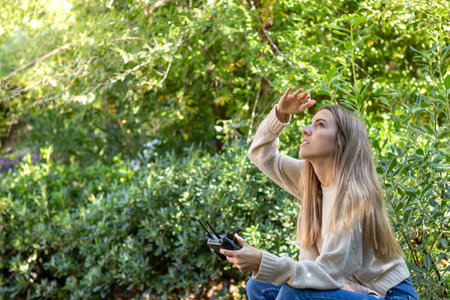 Young blonde woman trying to find the dronde while flying high away in nature with copy spaceの写真素材