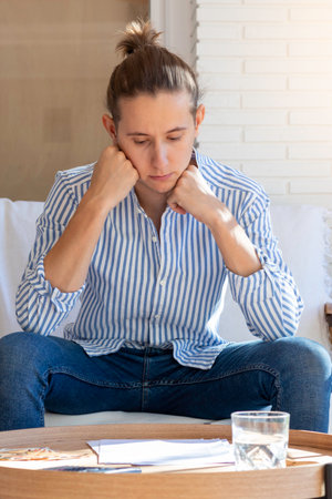 Vertical view of young man sitting in the sofa of the living room thoughtful while looking and reading at document on the wooden tableの写真素材