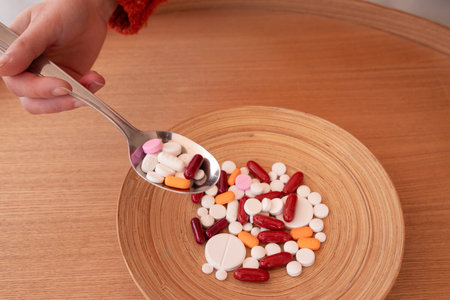 Crop woman having many pills and capsules with spoon served on wooden plate during lunch time at homeの写真素材