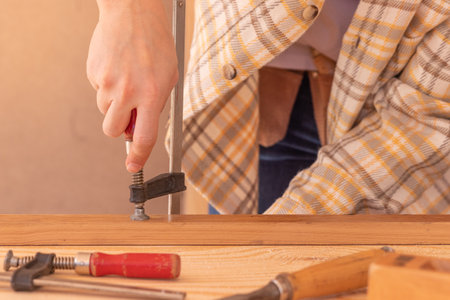 Craftsman with clamps working with wood. Crop unrecognizable male carpenter installing clamps and vices for gluing wooden details on workbenchの写真素材