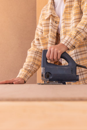 Unreconizable faceless Handy man working with jigsaw. Focused male woodworker in goggles cutting wooden board with electric jigsaw on workbenchの写真素材