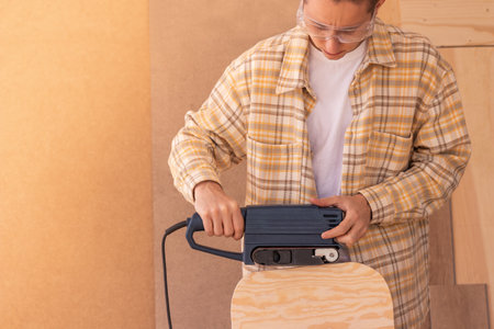 Repairman working with jigsaw in garage. Side view of crop unrecognizable male woodworker cutting wooden board with electric jigsawの写真素材