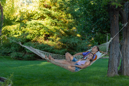 Couple relaxed laying in a white hammock in summer time in the green garden park in natural environment in the afternoonの写真素材