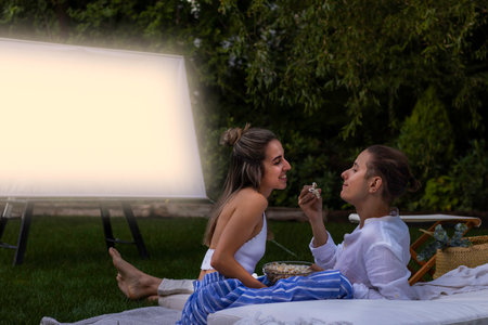 Happy and smiling girlfriend and boyfriend eating popcorns together in the outdoor cinema in summer nightの写真素材