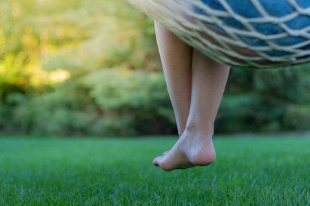 Unrecognizable woman cressed legs hanging from a hammock with the garden in the background in summerの写真素材