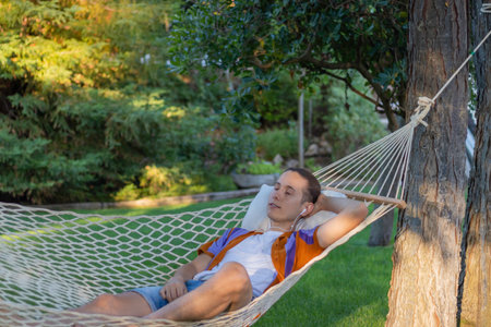 Young man on vacation lying in a hammock while listening to music calm and relaxed with nature in the background in summerの写真素材