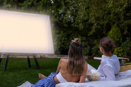 Unrecognizable young couple in love with their backs watching a movie in the garden in a summer night in the gardenの写真素材