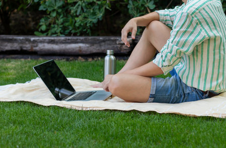 Unrecognizable young man sitting in the garden using the computer in his leisure time in summer weatherの写真素材