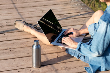 Side view of unrecognizable young man with straight leg working on his online job in natural environment in summerの写真素材