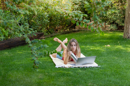 Top view of young woman lying in the garden working as a freelancer for her own online business in Europeの写真素材