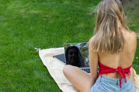 Back view of young woman reflected and using laptop in the garden in her leisure time to enjoy the good weather of summerの写真素材