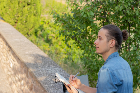 Side view of young hipster man looking to the side and drawing as hobby activity in the nature environmentの写真素材