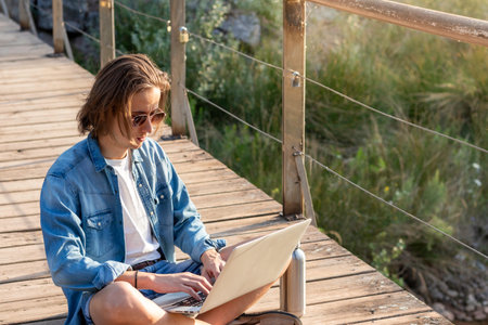 Portrait of young online working as freelancer man with long hair sitting on the floor working on his laptop while on vacationの写真素材