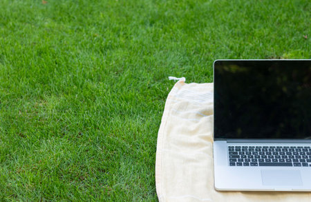 Cropped view of laptop leaning on a towel in the garden floor with green fresh grass in spring weatherの写真素材