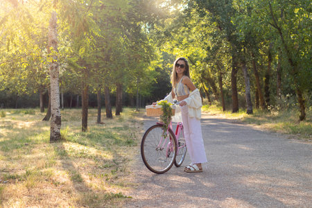 Young blonde woman looking to camera while riding a bicycle in the middle of the natural environment alone with no people aroundの写真素材