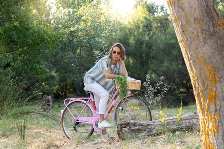 Young handsome man in sunglasses and long haired posing leaning on a pink retro bike with trees in the green backgroundの写真素材