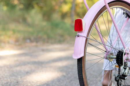 Closeup cropped view of pink bike from the back with a woman riding it on the road with nature and plants aroundの写真素材
